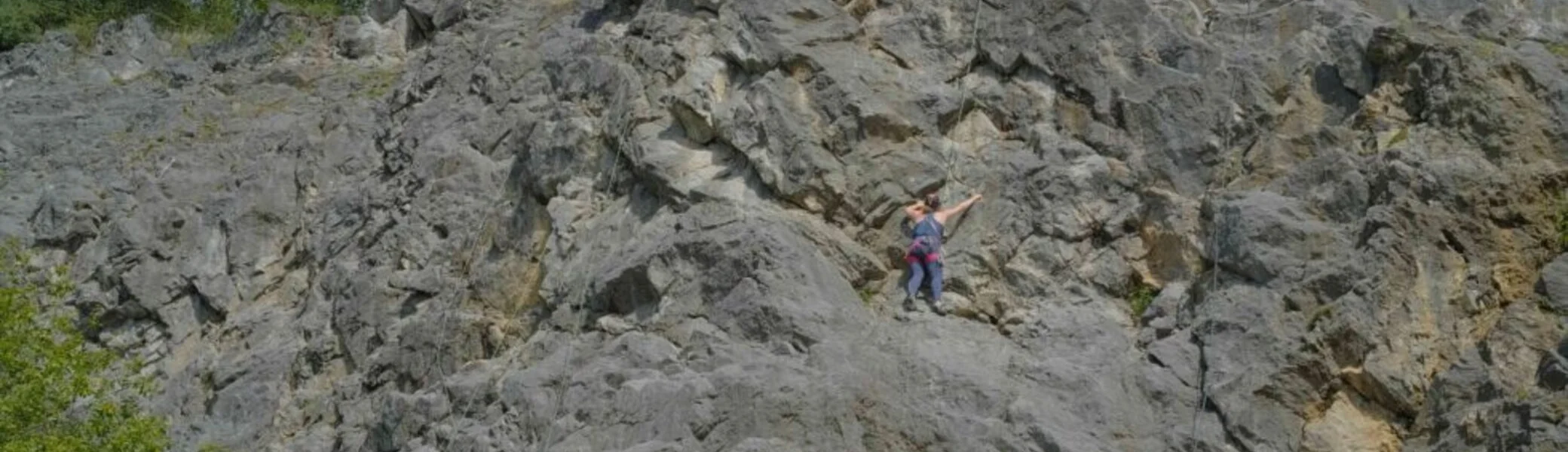 Mehrere Personen klettern an einer breiten grauen Kalkfelswand unter blauem Himmel. | © JDAV