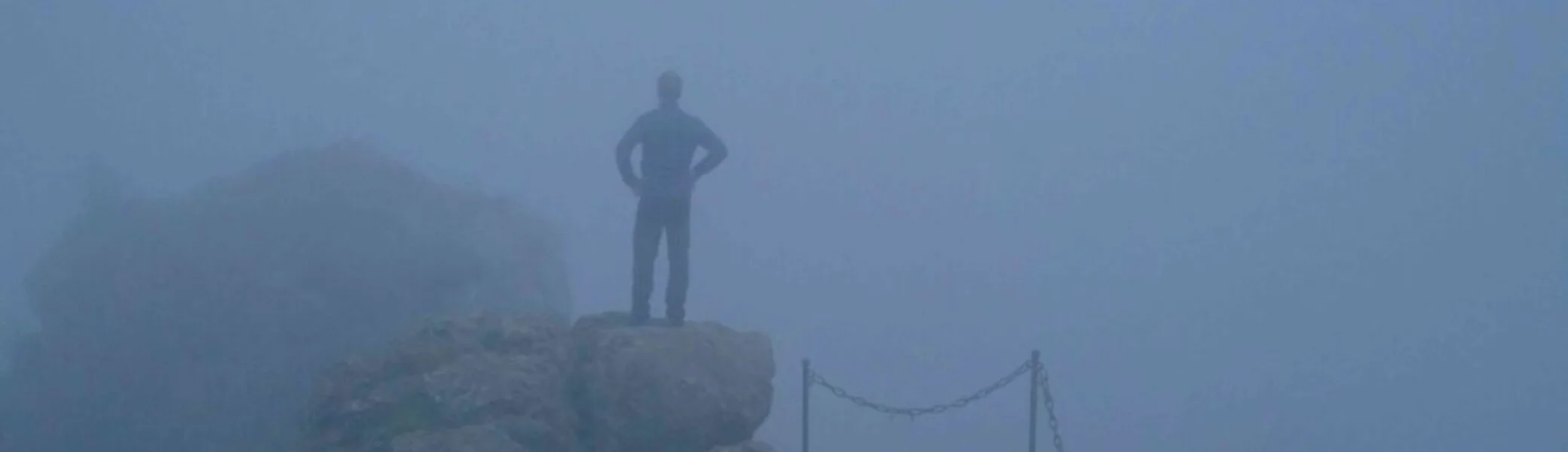 Einzelne Person steht auf einem Felsen im Nebel, die Umgebung ist kaum sichtbar. | © JDAV