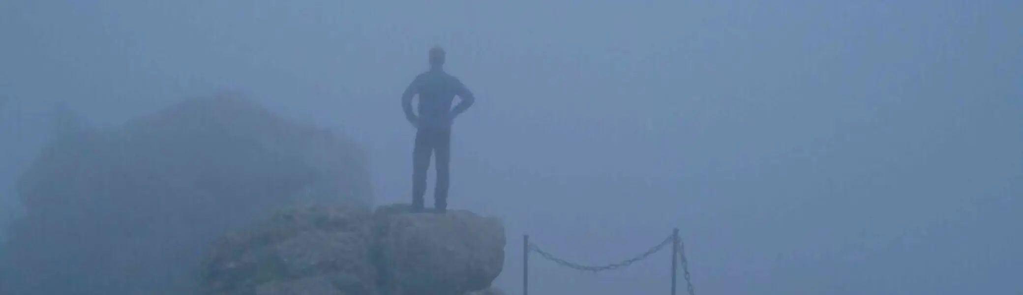 Einzelne Person steht auf einem Felsen im Nebel, die Umgebung ist kaum sichtbar. | © JDAV