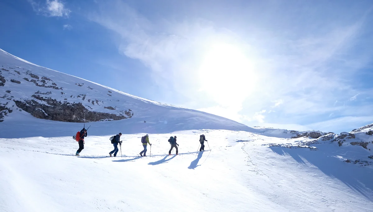 Fünf Skitourengeher*innen steigen bei Sonne eine verschneite Anhöhe hinauf | © DAV Dortmund