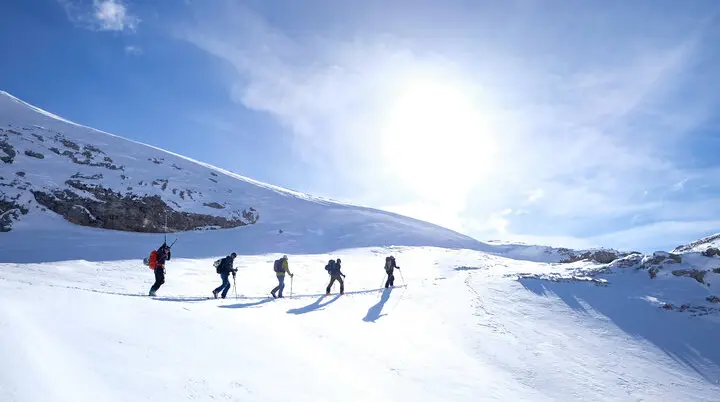 Fünf Skitourengeher*innen steigen bei Sonne eine verschneite Anhöhe hinauf | © DAV Dortmund