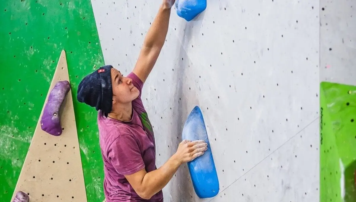 Ein junger Mann klettert an einer Indoor-Boulderwand mit großen blauen Griffen. | © DAV Dortmund