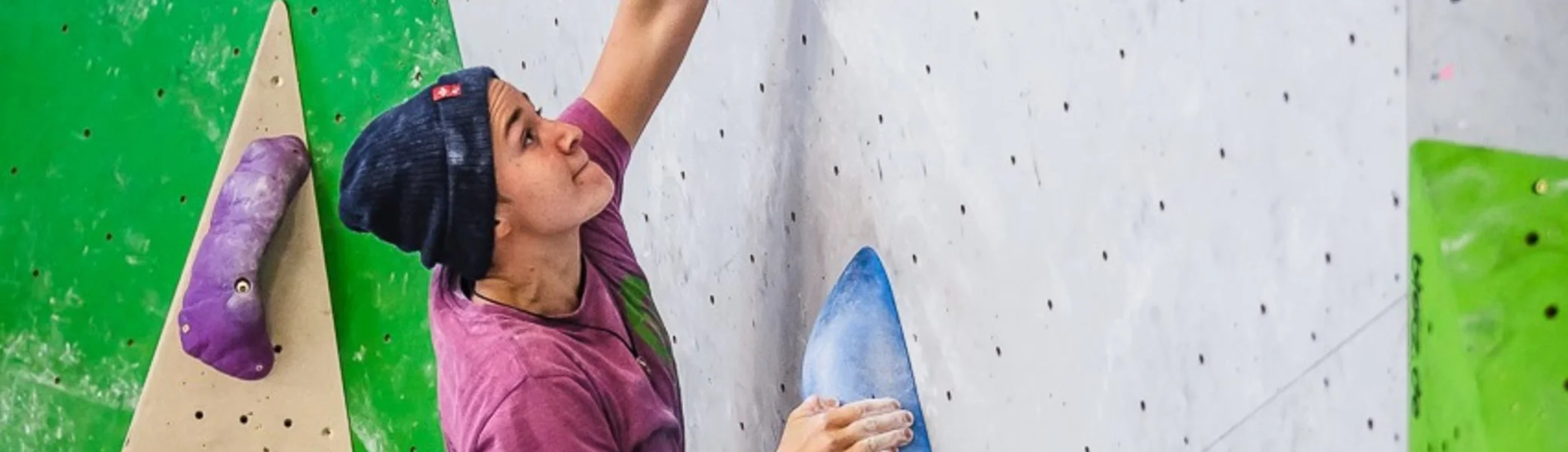 Ein junger Mann klettert an einer Indoor-Boulderwand mit großen blauen Griffen. | © DAV Dortmund