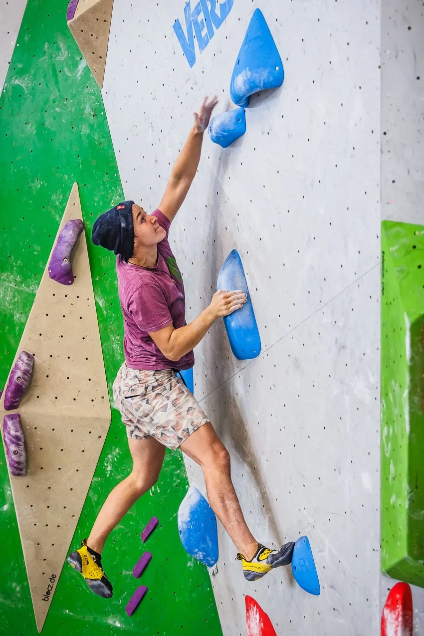 Ein junger Mann klettert an einer Indoor-Boulderwand mit großen blauen Griffen. | © DAV Dortmund