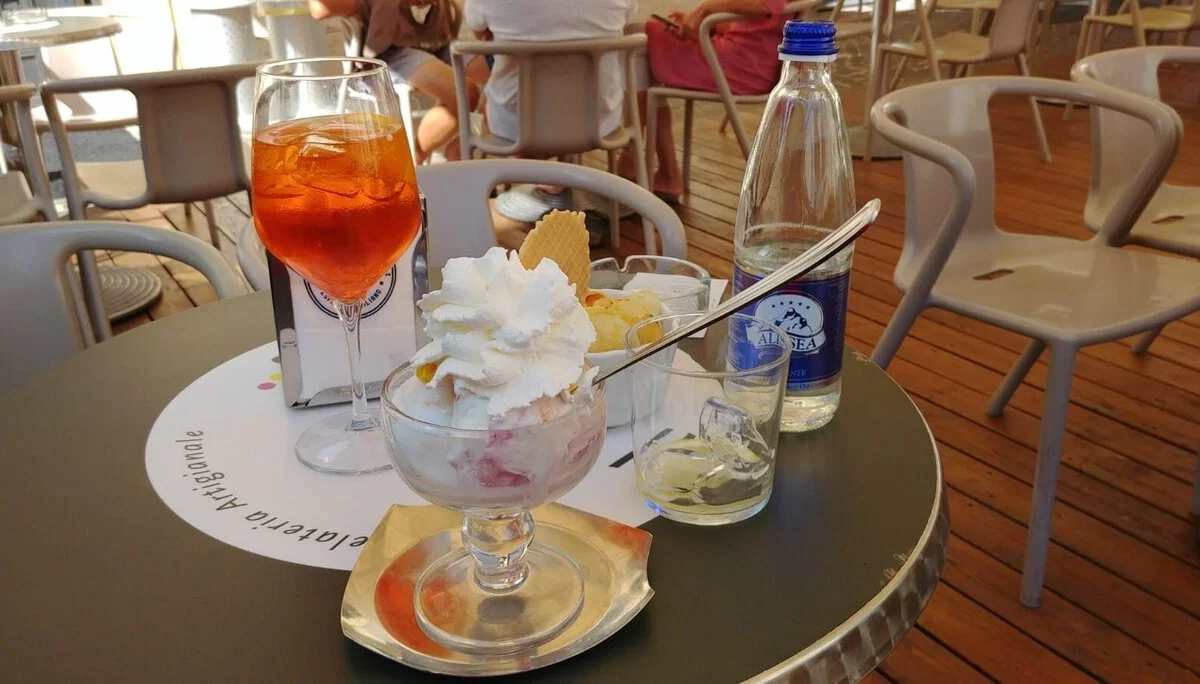 Auf einem Tisch stehen ein Eisbecher mit Sahne, ein Getränk und eine Wasserflasche im Straßencafé. | © DAV Dortmund