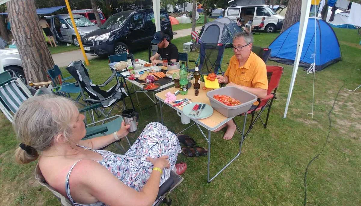 Zwei Personen sitzen unter einem Pavillon an einem gedeckten Campingtisch auf einem Zeltplatz. | © DAV Dortmund