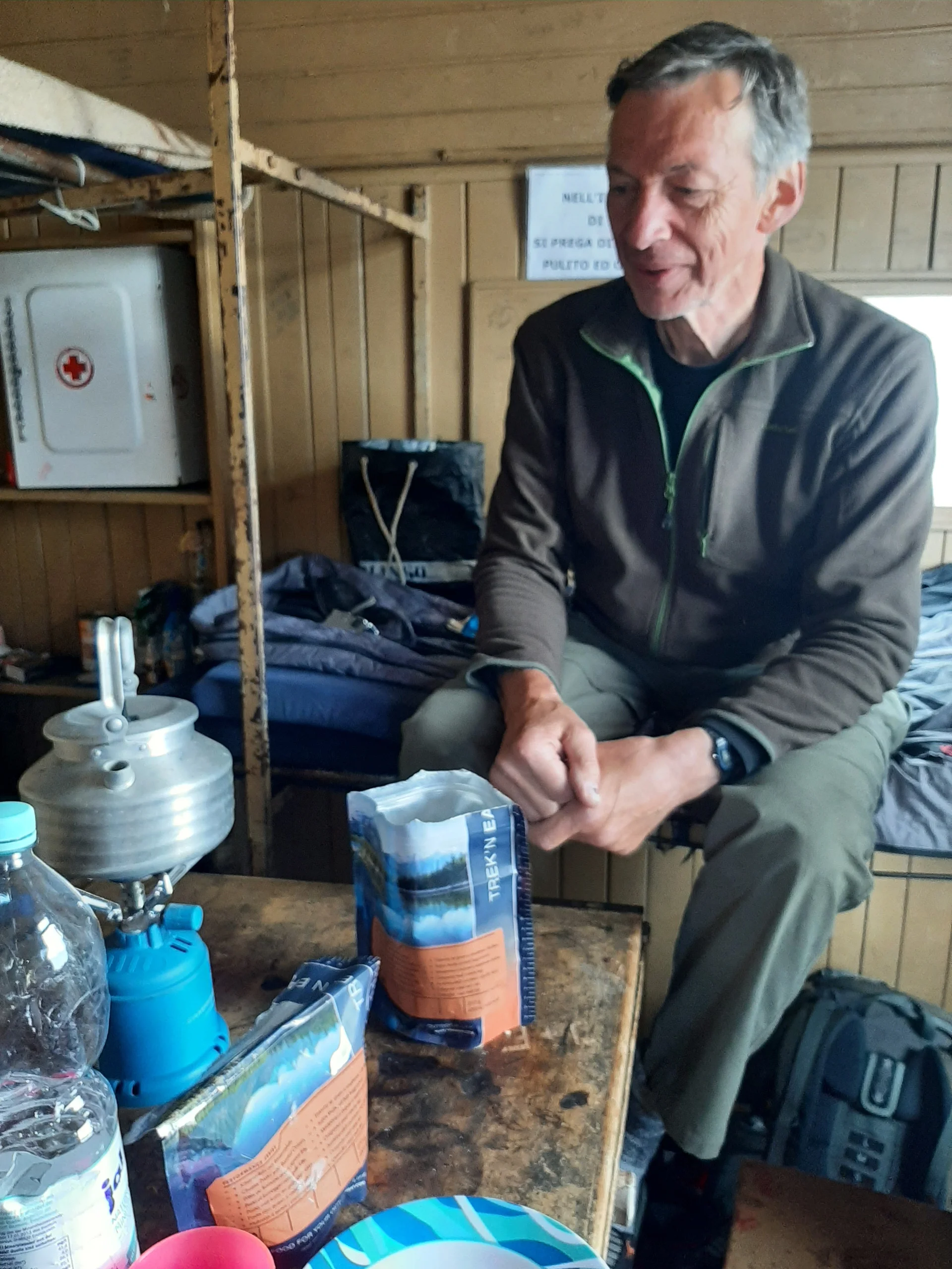 Eine Person sitzt an einem Tisch in einer einfachen Holzhütte mit Trekkingnahrung und Kocher. | © DAV Dortmund
