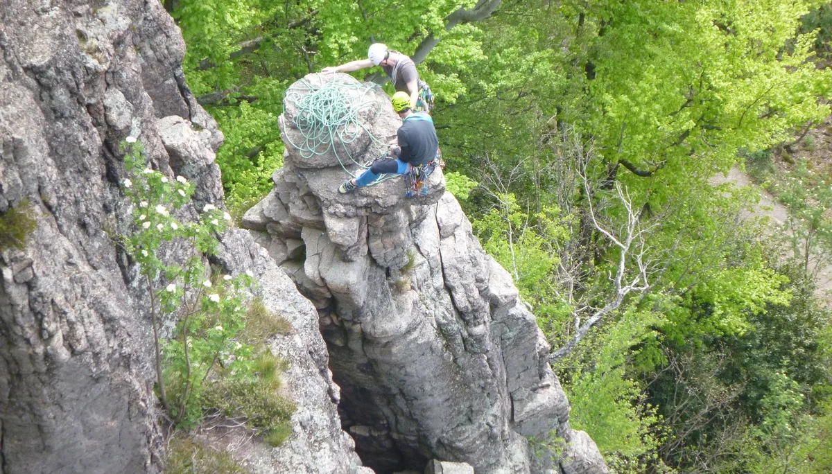 Zwei Personen stehen mit Seil und Ausrüstung auf einem Felsvorsprung im Waldgebiet. | © DAV Dortmund