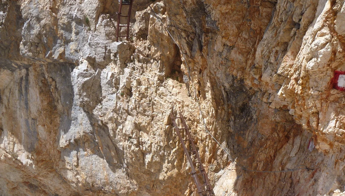 Zwei Personen steigen eine senkrechte Metallleiter in einer rötlichen Felswand hinauf. | © DAV Dortmund