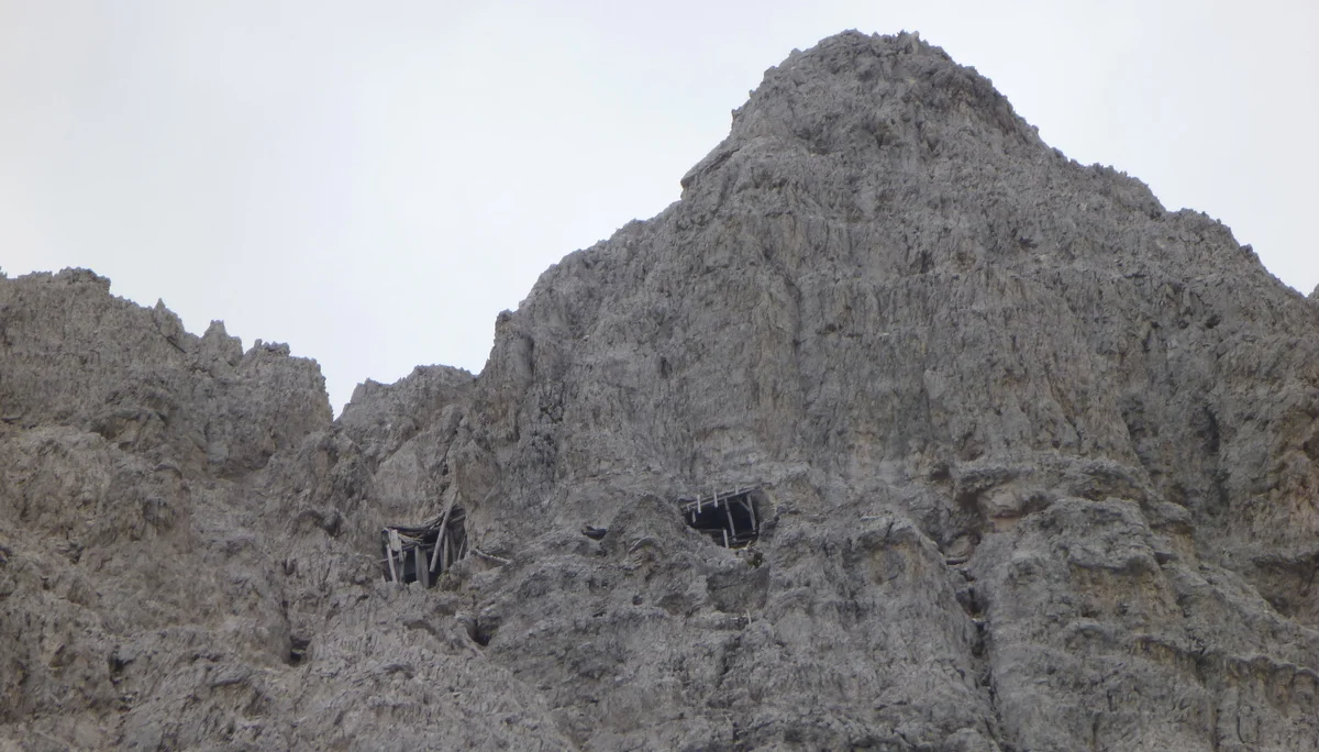 Blick auf eine hohe graue Felswand mit zwei alten Kriegsstellungen oder Bunkereingängen. | © DAV Dortmund