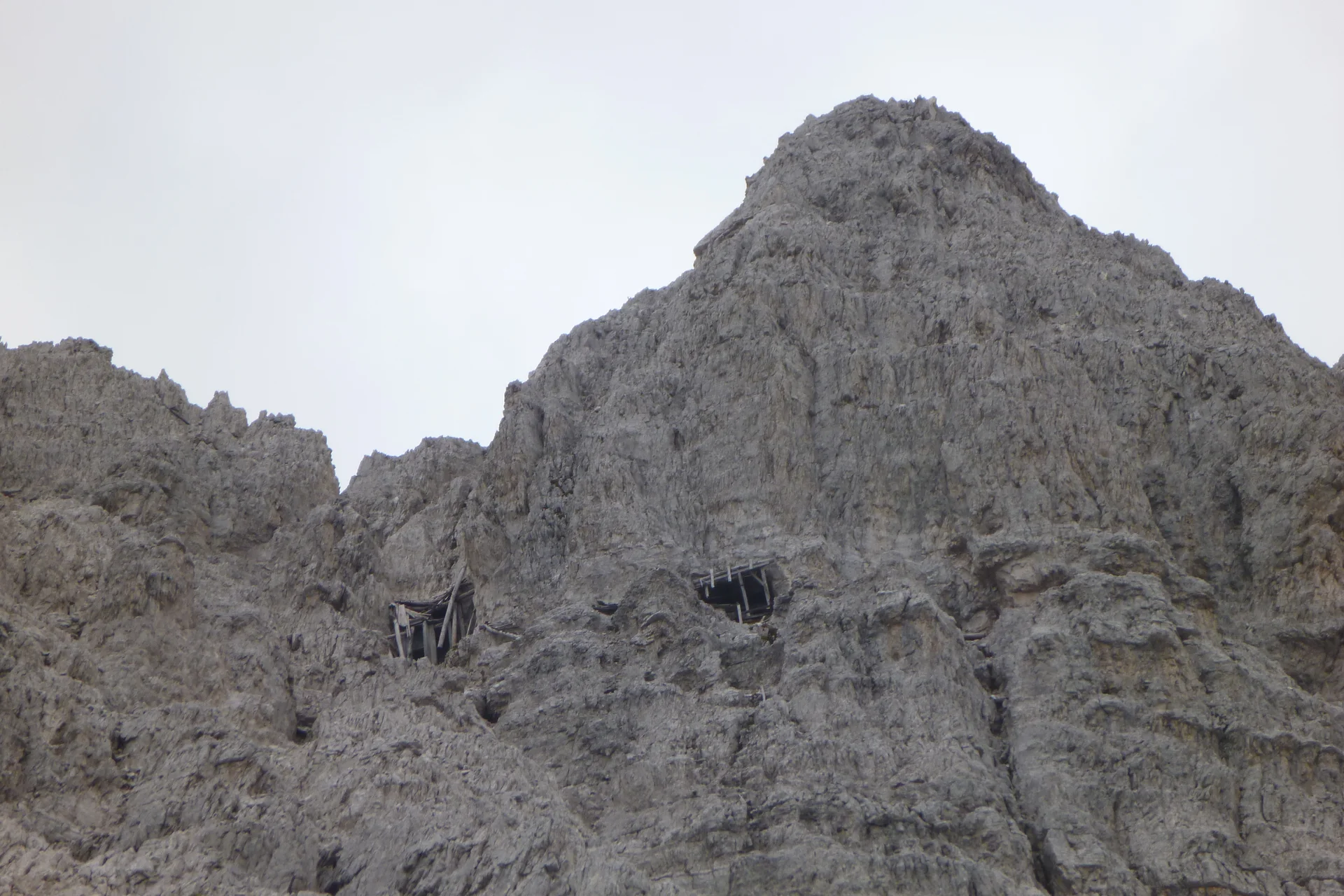 Blick auf eine hohe graue Felswand mit zwei alten Kriegsstellungen oder Bunkereingängen. | © DAV Dortmund