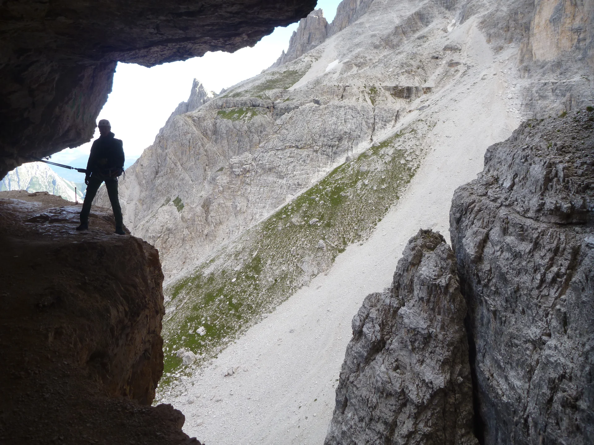 Eine Person steht am Eingang einer Felsgrotte mit Blick auf eine steile Geröllflanke in den Dolomiten. | © DAV Dortmund