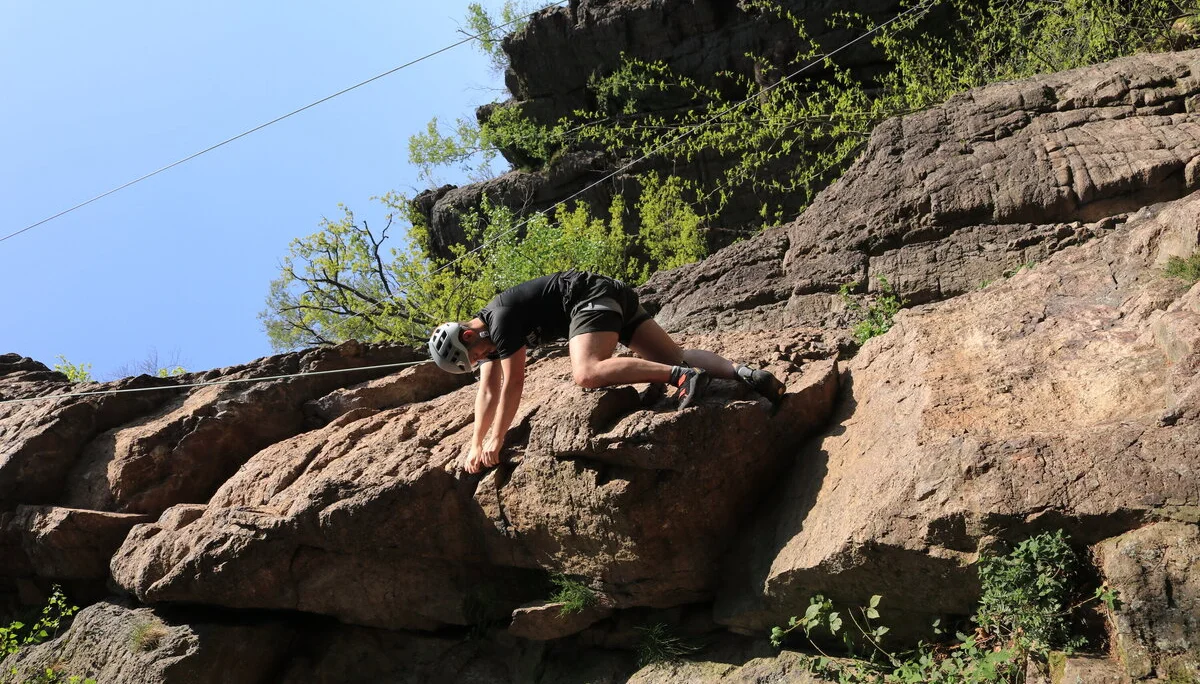 Ein Kletterer mit Helm erklimmt bei Sonnenschein eine steile Felswand in einem bewaldeten Gebiet. | © DAV Dortmund