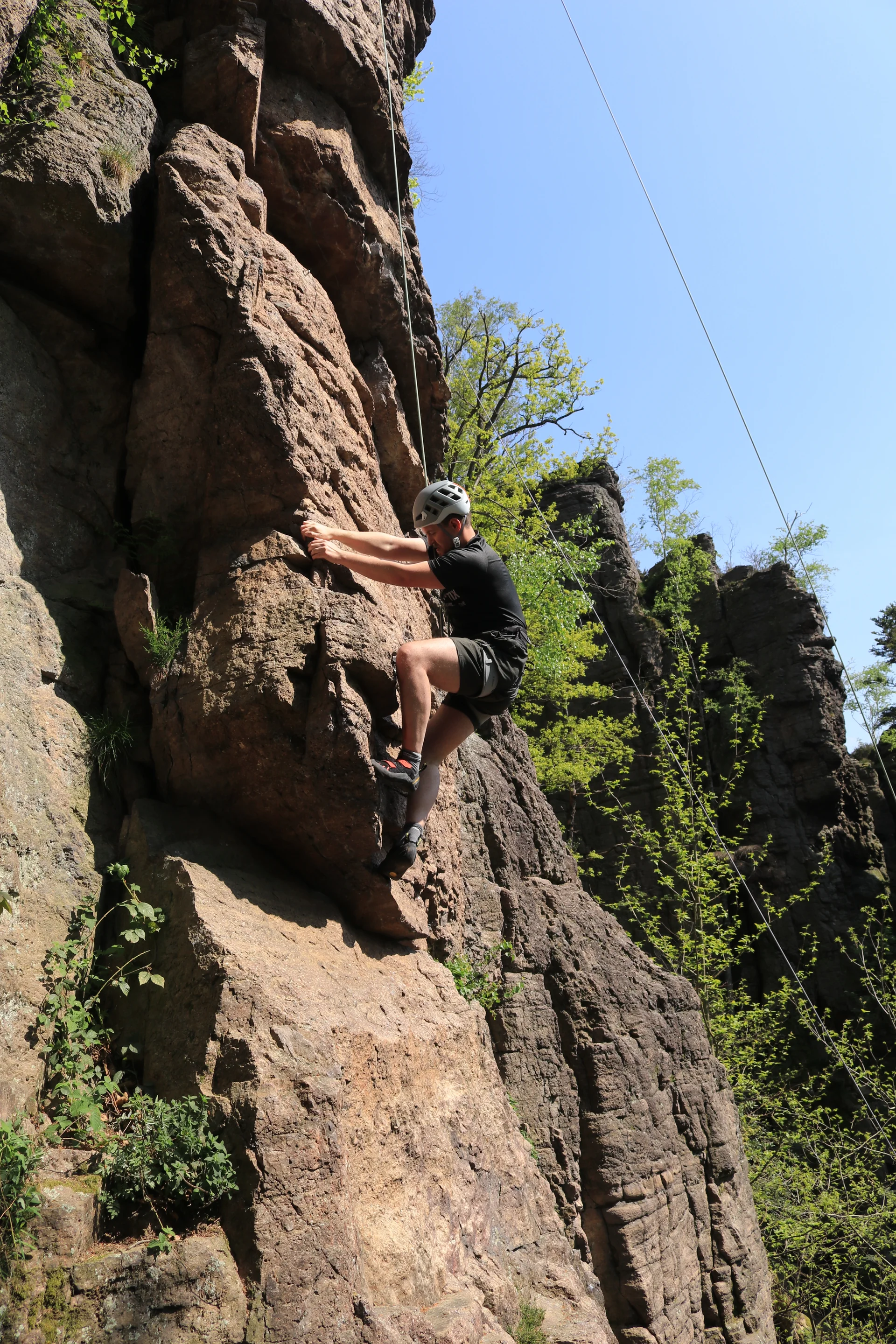 Ein Kletterer mit Helm erklimmt bei Sonnenschein eine steile Felswand in einem bewaldeten Gebiet. | © DAV Dortmund