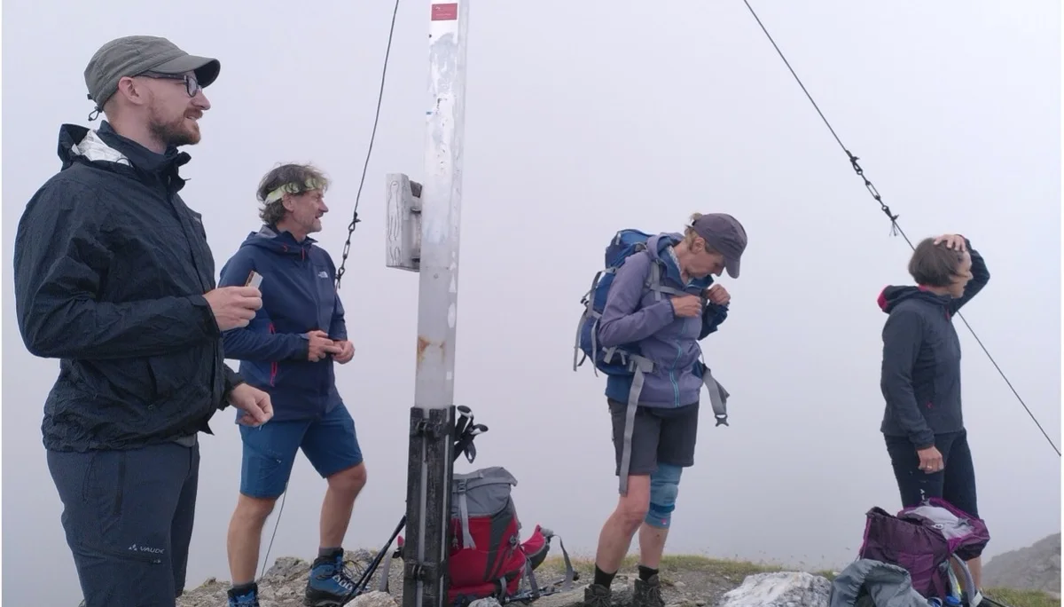 Fünf Wandernde stehen am Gipfelkreuz bei dichter Nebelstimmung, umgeben von Ausrüstung. | © DAV Dortmund