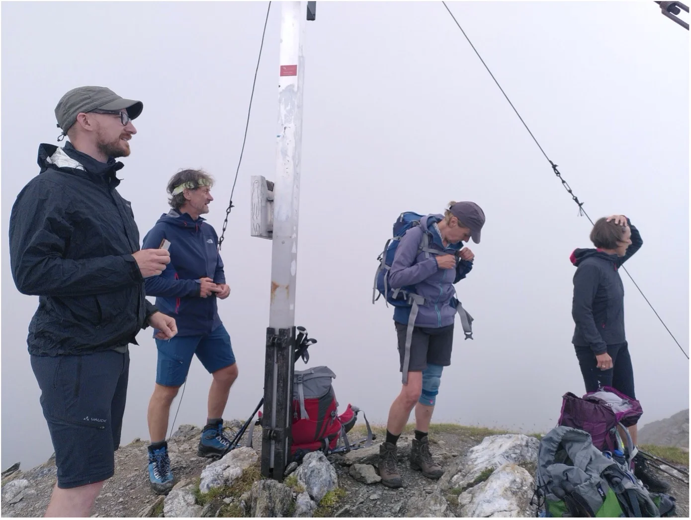 Fünf Wandernde stehen am Gipfelkreuz bei dichter Nebelstimmung, umgeben von Ausrüstung. | © DAV Dortmund
