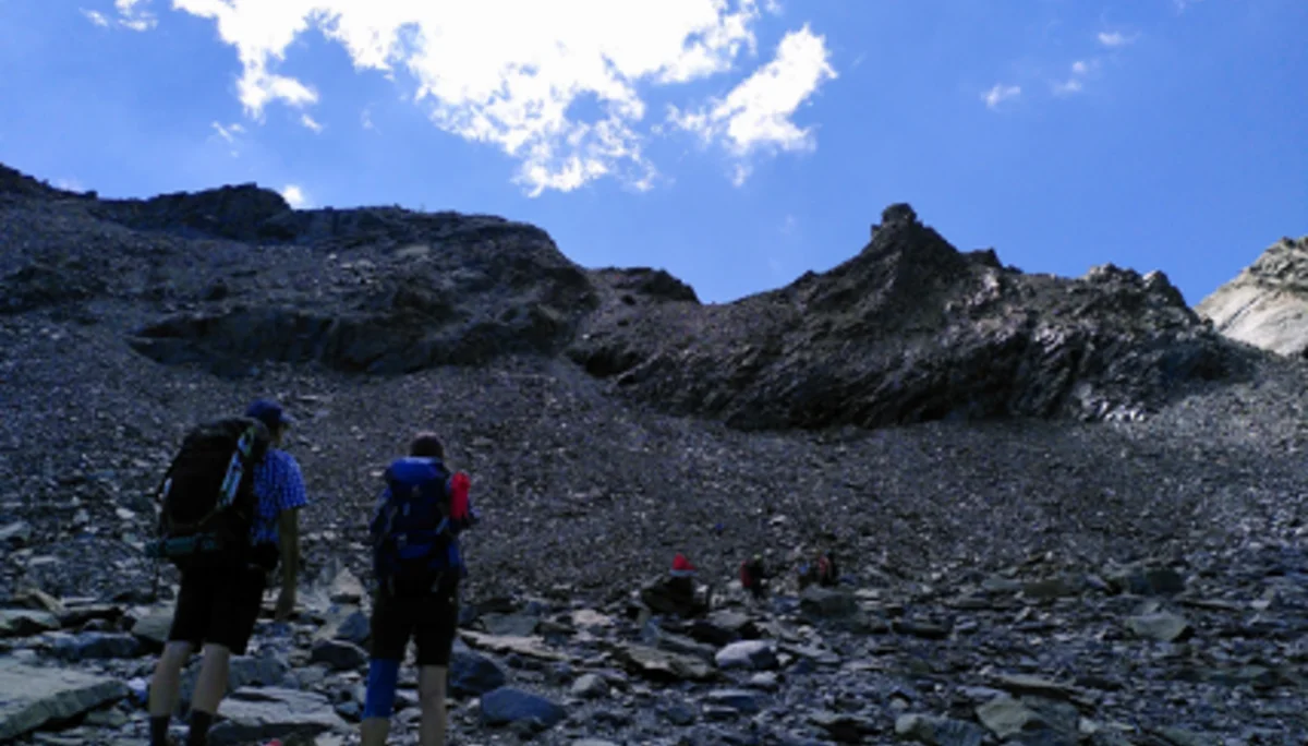 Wanderer steigen über steiniges Gelände in Richtung felsiger Gipfel bei blauem Himmel. | © DAV Dortmund