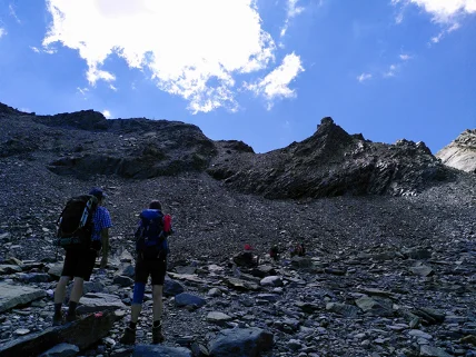 Wanderer steigen über steiniges Gelände in Richtung felsiger Gipfel bei blauem Himmel. | © DAV Dortmund