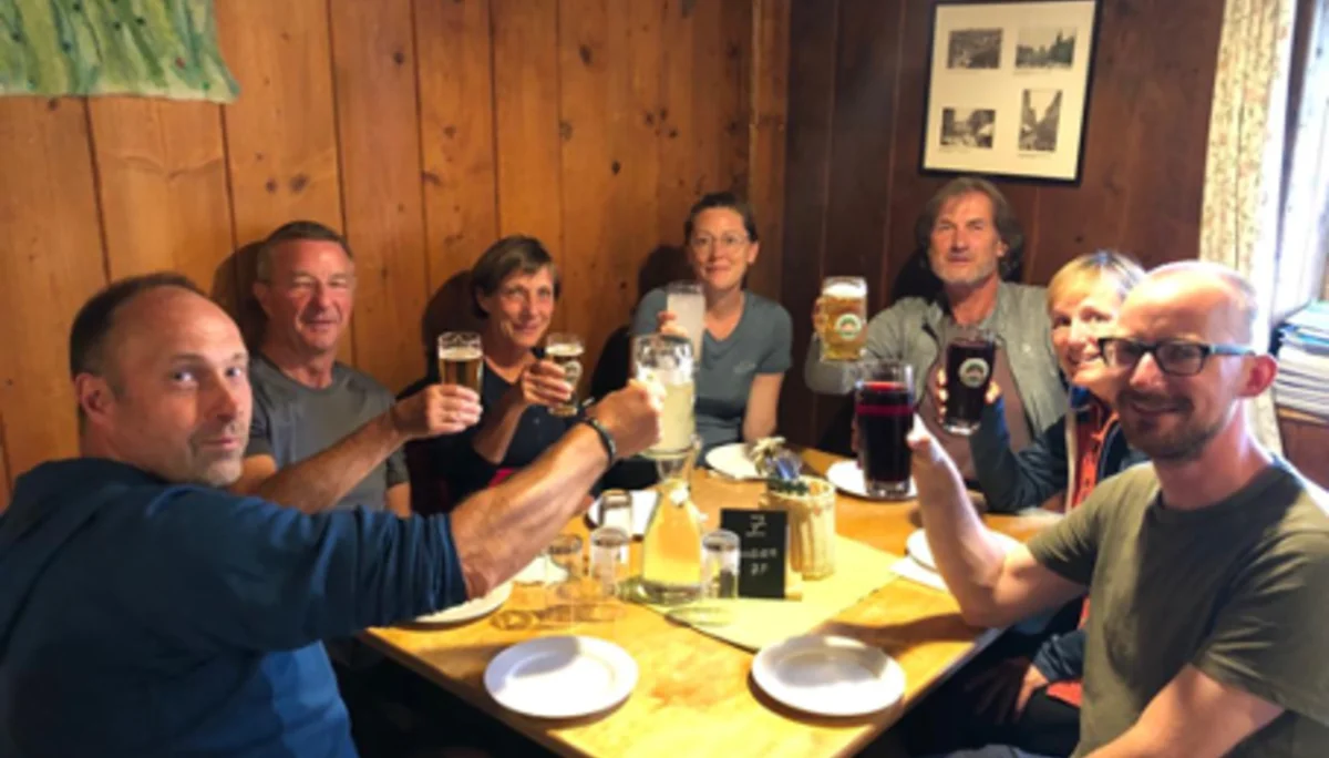 Sieben Personen sitzen an einem Holztisch in einer Berghütte und stoßen mit Getränken an. | © DAV Dortmund