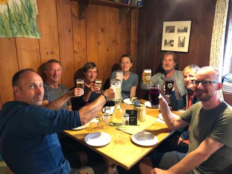 Sieben Personen sitzen an einem Holztisch in einer Berghütte und stoßen mit Getränken an. | © DAV Dortmund
