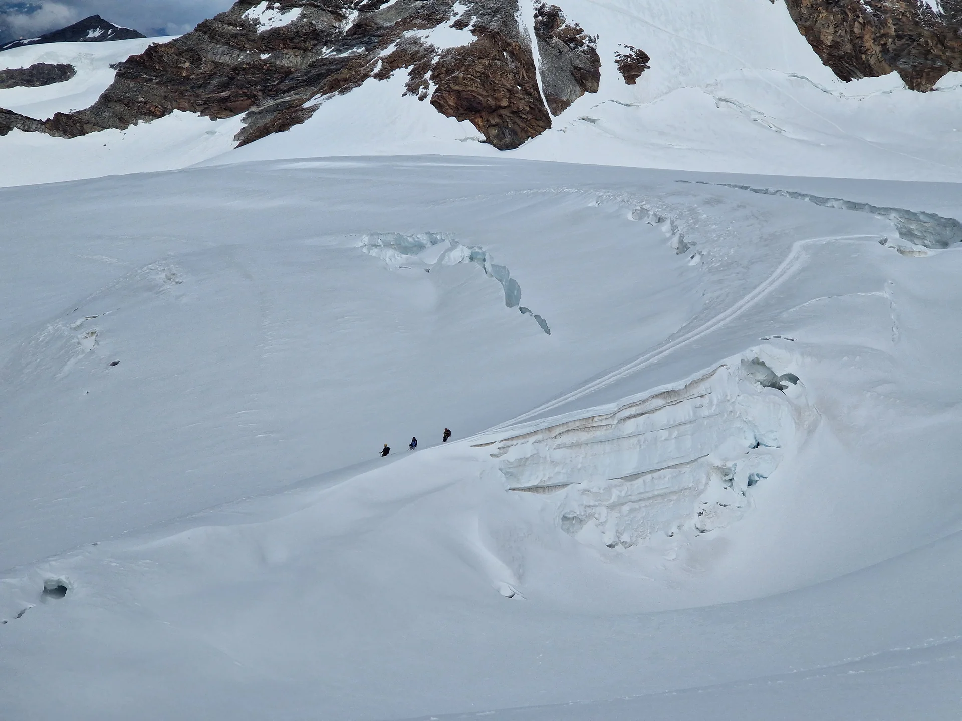 Drei Bergsteiger*innen bewegen sich gesichert in einer Seilschaft über einen schneebedeckten Gletscher, umgeben von großen Gletscherspalten und Felsformationen. | © DAV Dortmund