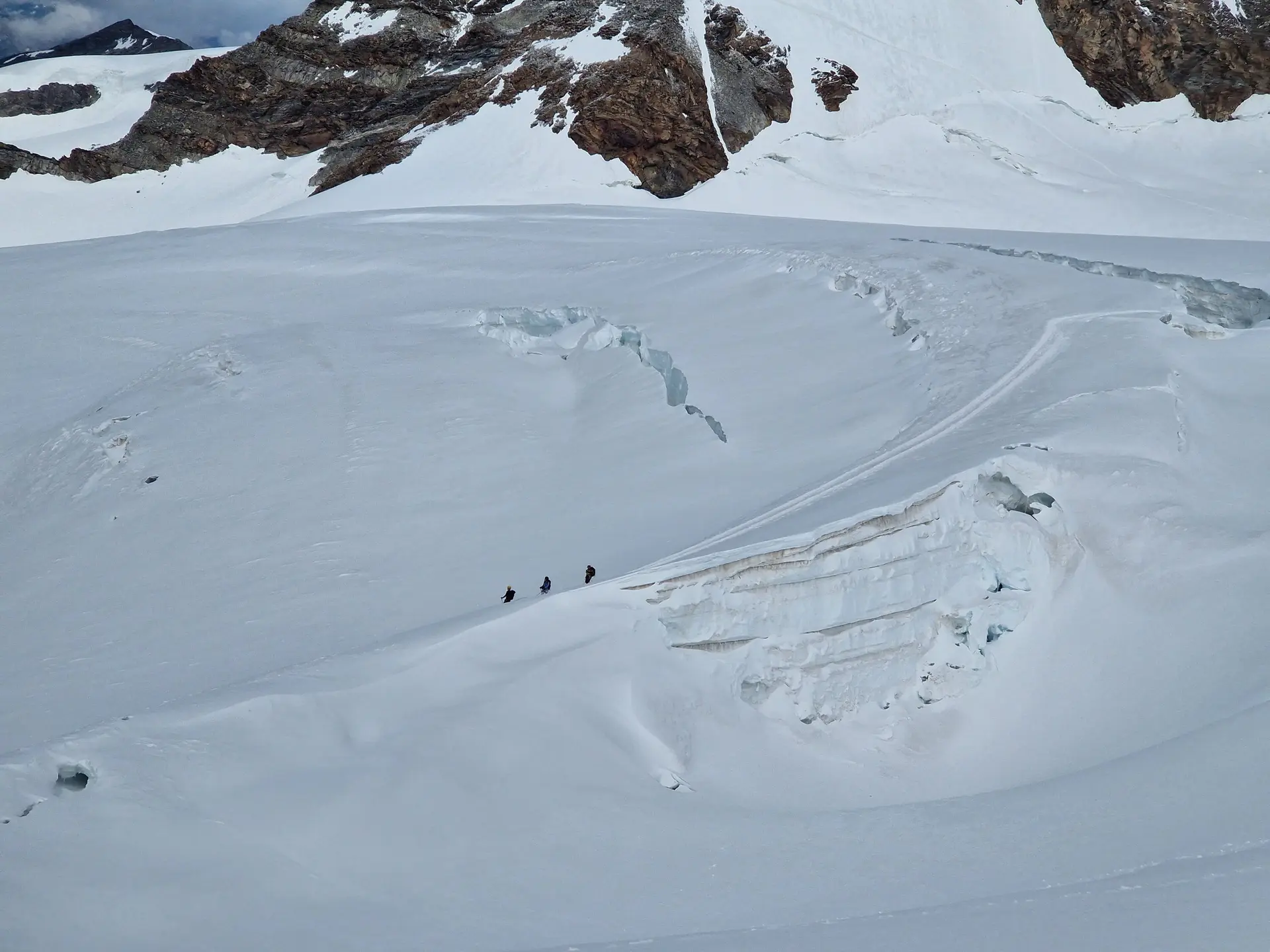 Drei Bergsteiger*innen bewegen sich gesichert in einer Seilschaft über einen schneebedeckten Gletscher, umgeben von großen Gletscherspalten und Felsformationen. | © DAV Dortmund