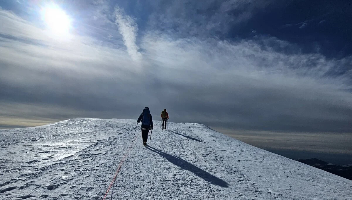 Zwei Bergsteiger*innen steigen angeseilt über einen sonnenbeschienenen, verschneiten Grat, während die Sonne tief am Himmel steht und lange Schatten wirft. | © DAV Dortmund