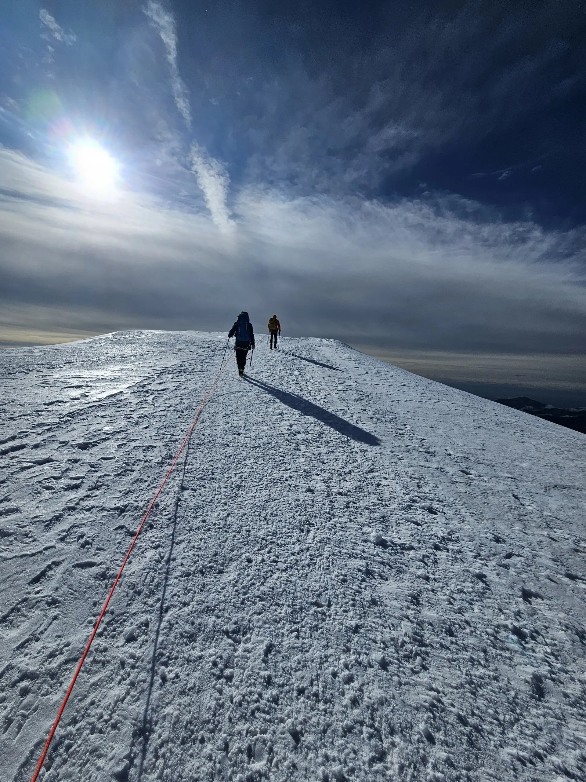 Zwei Bergsteiger*innen steigen angeseilt über einen sonnenbeschienenen, verschneiten Grat, während die Sonne tief am Himmel steht und lange Schatten wirft. | © DAV Dortmund