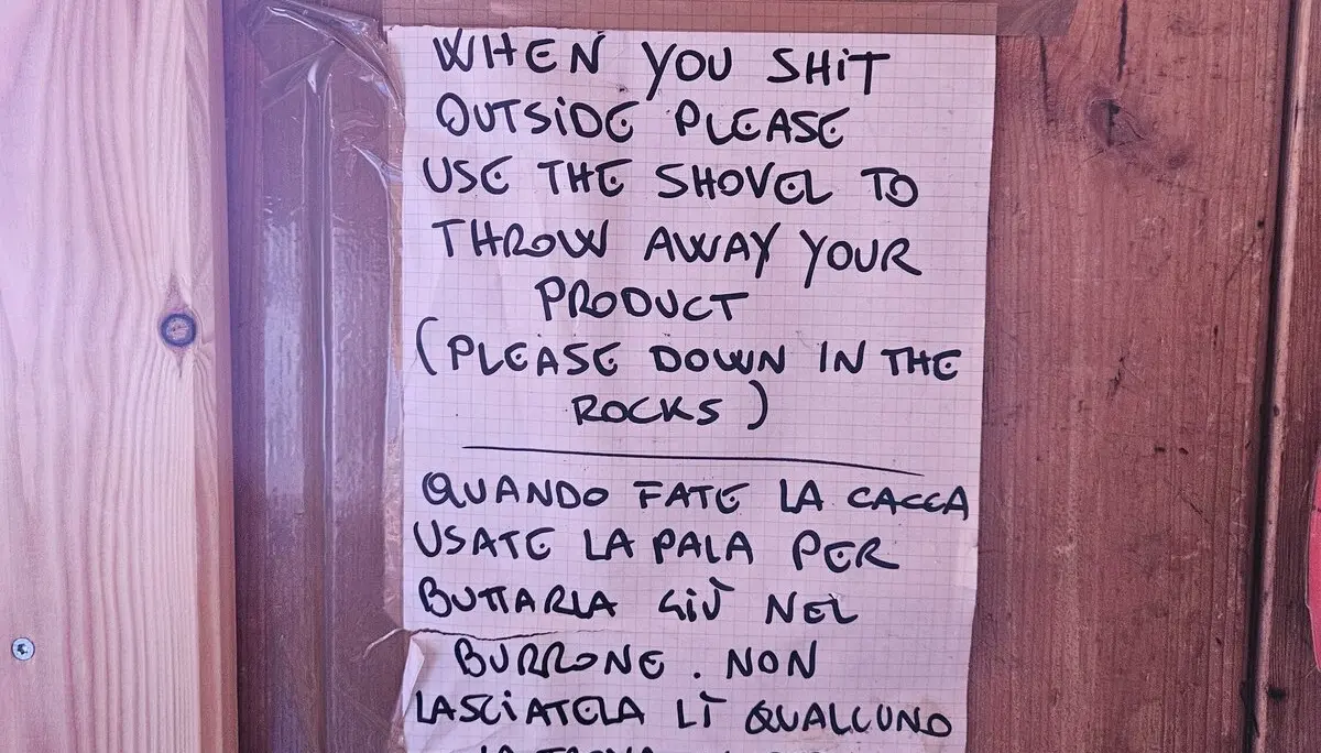 Handgeschriebener Zettel an einer Holzwand, der Besucher auffordert, beim Toilettengang draußen eine Schaufel zu benutzen und die Hinterlassenschaft in den Felsen zu entsorgen. Text auf Englisch und Italienisch. | © DAV Dortmund