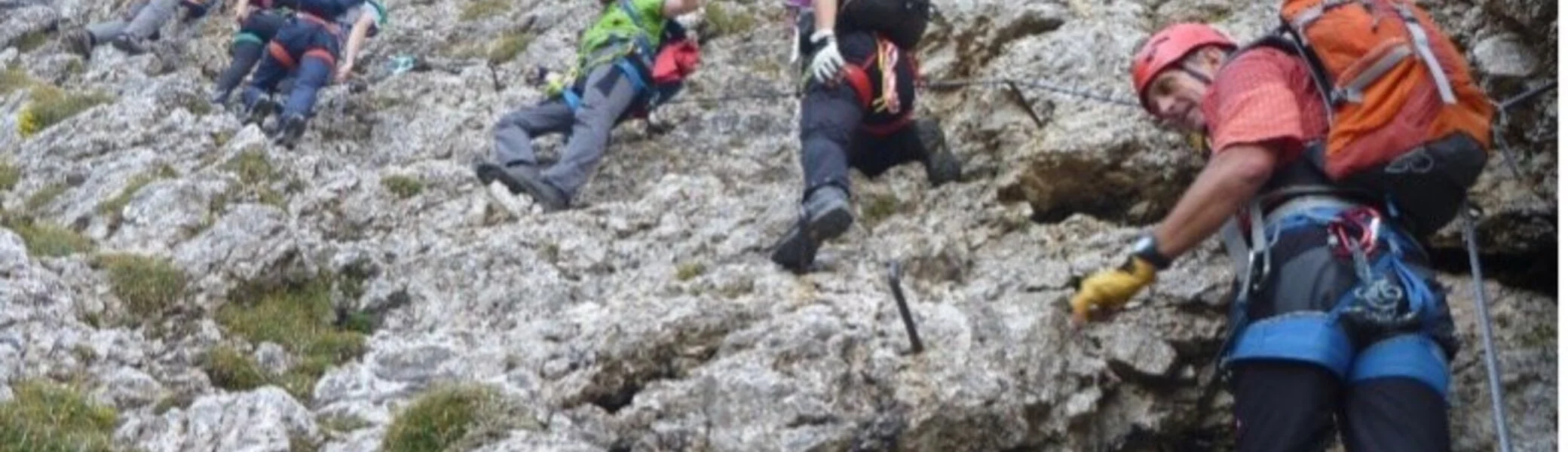 Eine größere Gruppe bewegt sich mit Kletterausrüstung schräg über eine steile Felswand. | © DAV Dortmund