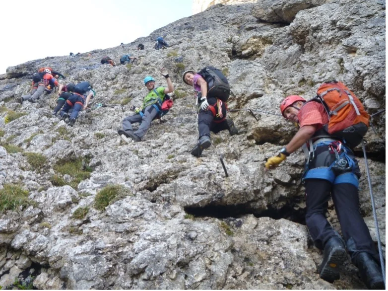 Eine größere Gruppe bewegt sich mit Kletterausrüstung schräg über eine steile Felswand. | © DAV Dortmund