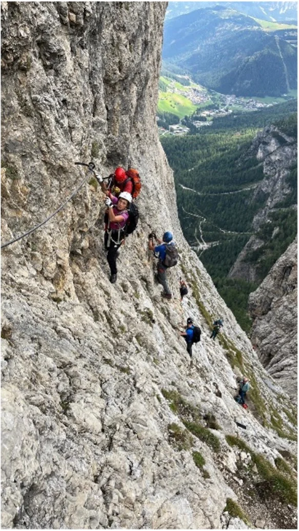 Mehrere Personen mit Helm und Gurt klettern gesichert an einem steilen Klettersteig mit Blick ins Tal. | © DAV Dortmund