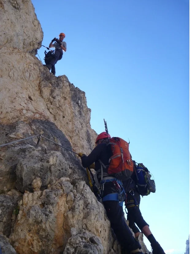 Zwei Personen klettern mit Klettersteigset an einer steilen Felswand im Gegenlicht. | © DAV Dortmund