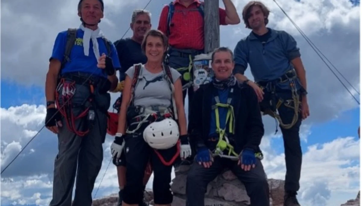 Sechs Personen stehen in Kletterausrüstung lachend am Gipfelkreuz unter wolkigem Himmel. | © DAV Dortmund