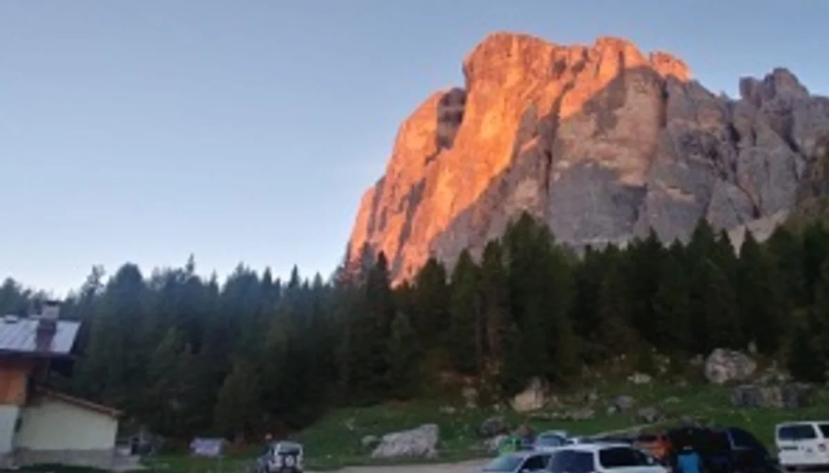Eine markante Felswand leuchtet rötlich in der Abendsonne, im Vordergrund ein Parkplatz mit Fahrzeugen. | © DAV Dortmund