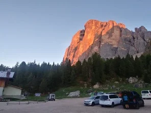 Eine markante Felswand leuchtet rötlich in der Abendsonne, im Vordergrund ein Parkplatz mit Fahrzeugen. | © DAV Dortmund