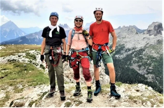 Drei Personen in Kletterausrüstung stehen nebeneinander auf einem Berg mit Ausblick auf die Dolomiten. | © DAV Dortmund