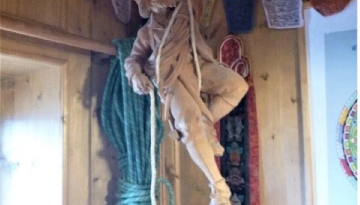 Eine Holzfigur eines Kletterers hängt an einem Seil von der Decke einer gemütlichen Berghütte. | © DAV Dortmund