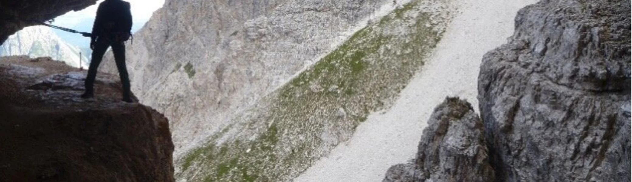 Eine Person steht am Rand einer Felsgrotte mit Blick auf schroffe Berghänge im Hintergrund. | © DAV Dortmund