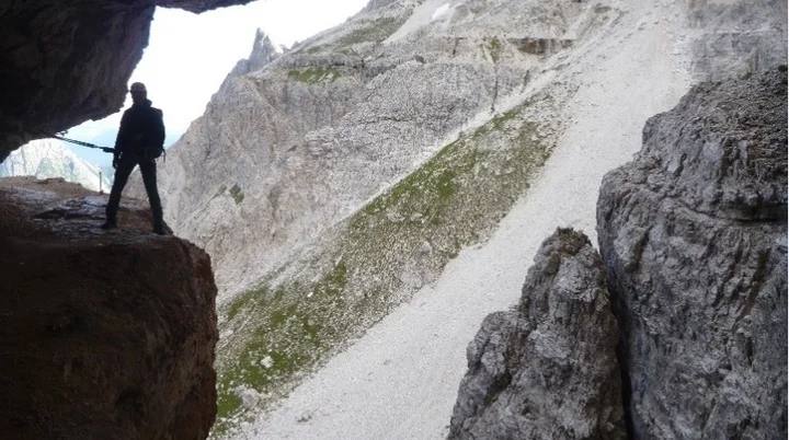 Eine Person steht am Rand einer Felsgrotte mit Blick auf schroffe Berghänge im Hintergrund. | © DAV Dortmund