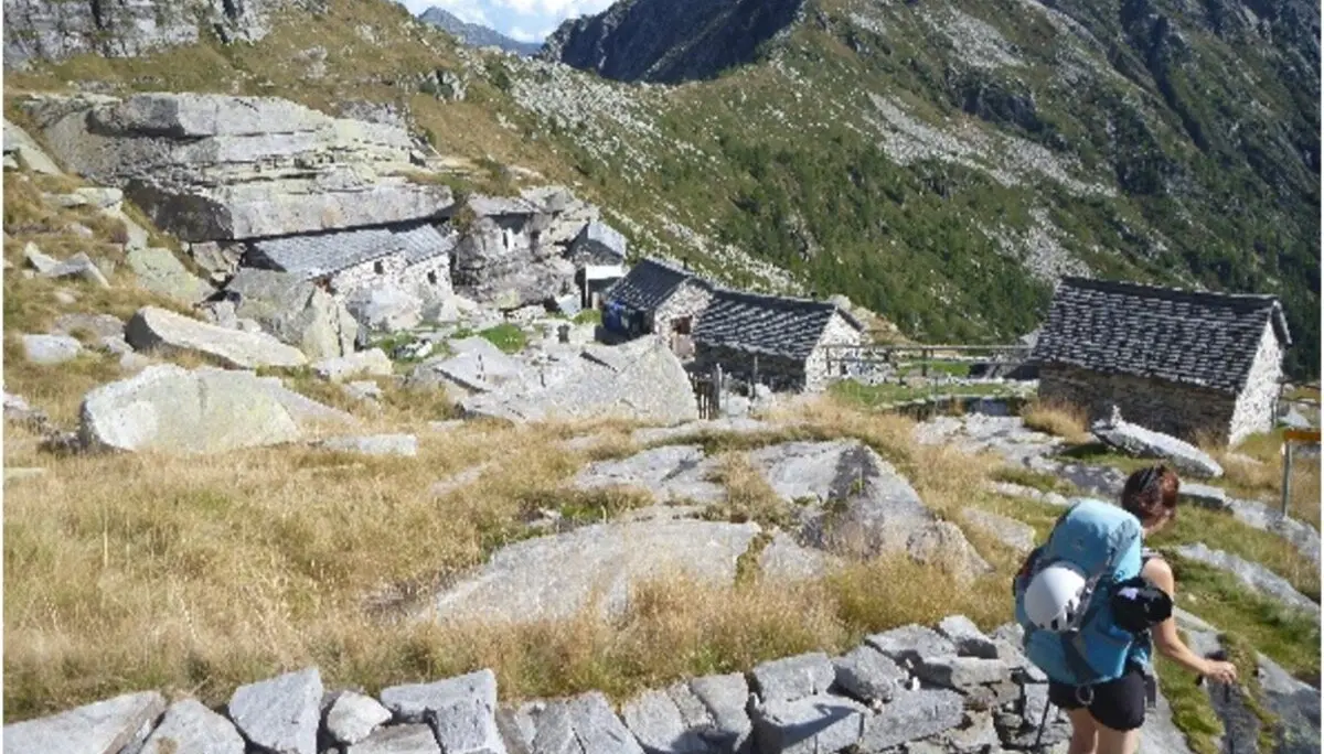Wandernde Person durchquert ein abgelegenes Steindorf in einer alpinen Landschaft mit steilen Hängen. | © DAV Dortmund