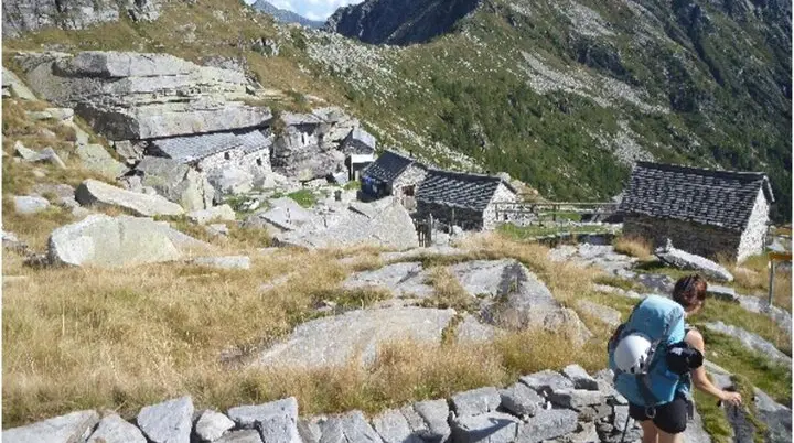 Wandernde Person durchquert ein abgelegenes Steindorf in einer alpinen Landschaft mit steilen Hängen. | © DAV Dortmund