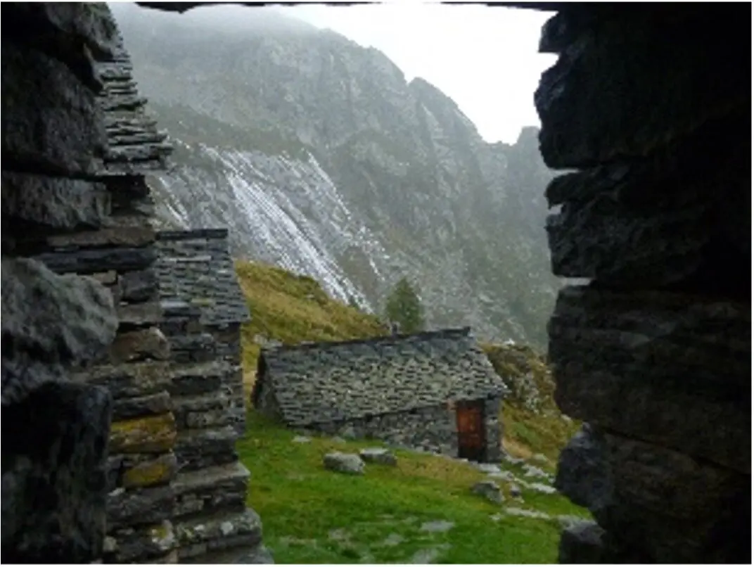 Blick aus einem Steinhaus auf weitere alte Steinhütten in nebeliger und regnerischer Gebirgslandschaft. | © DAV Dortmund
