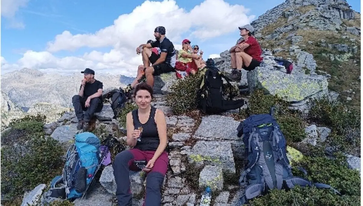 Wandergruppe sitzt und liegt auf einem felsigen Gipfel mit toller Aussicht, umgeben von Rucksäcken. | © DAV Dortmund