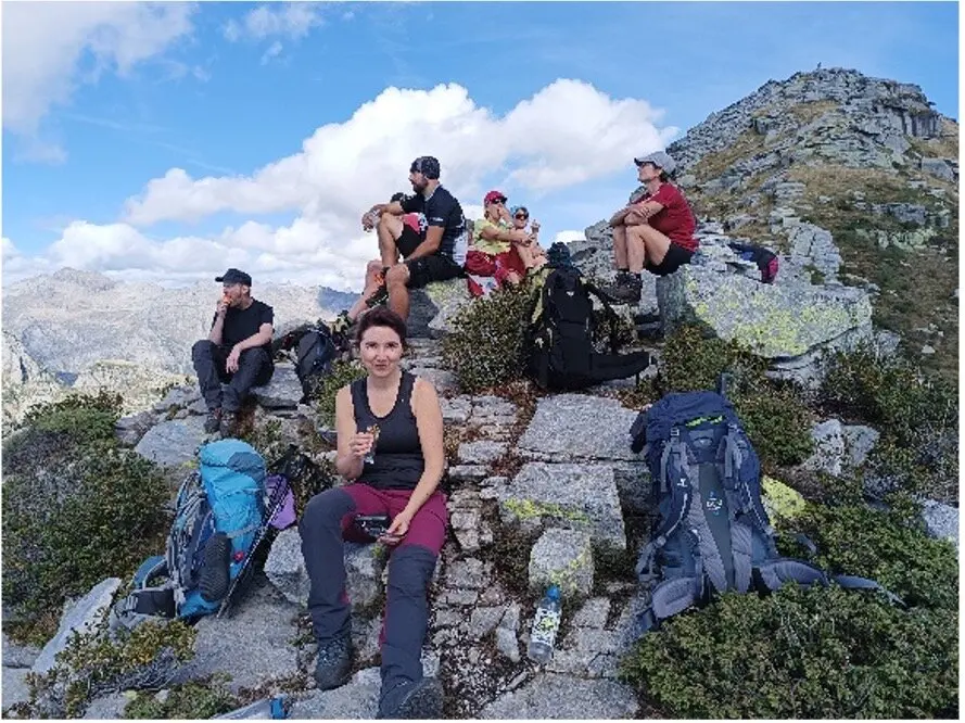 Wandergruppe sitzt und liegt auf einem felsigen Gipfel mit toller Aussicht, umgeben von Rucksäcken. | © DAV Dortmund