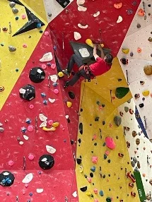 Eine Person klettert in einer bunten Kletterhalle an einer steilen, überhängenden Wand mit roten und gelben Griffen. | © DAV Dortmund