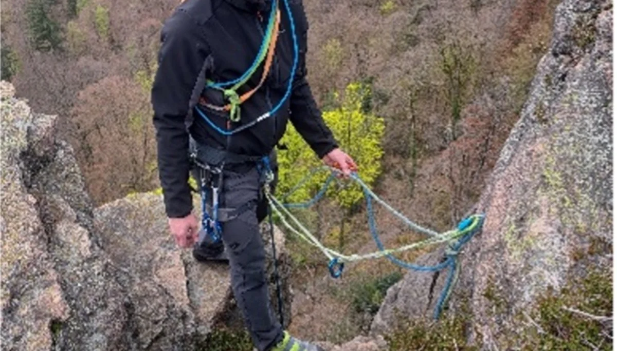 Eine Person mit Kletterhelm und Klettergurt steht auf einem Felsgrat mit Ausblick auf ein bewaldetes Tal. | © DAV Dortmund