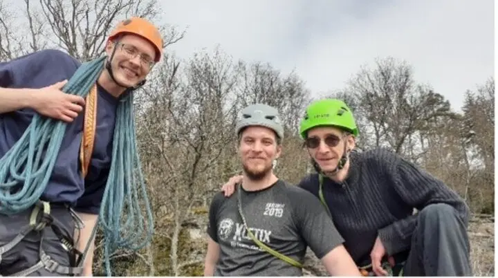Drei Männer mit Kletterausrüstung und Helmen lächeln in die Kamera beim Felsklettern. | © DAV Dortmund