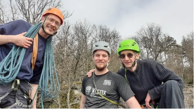 Drei Männer mit Kletterausrüstung und Helmen lächeln in die Kamera beim Felsklettern. | © DAV Dortmund