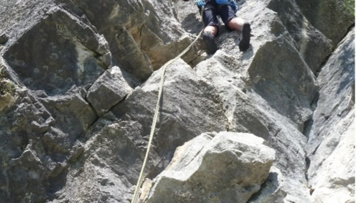 Eine Person seilt sich an einer steilen, zerklüfteten Felswand mit Sicherung ab. | © DAV Dortmund